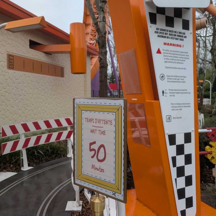 A sign at the RC Racer attraction displaying a 'WAIT TIME 50 Minutes' estimate. The sign also shows ride safety warnings in English and French.