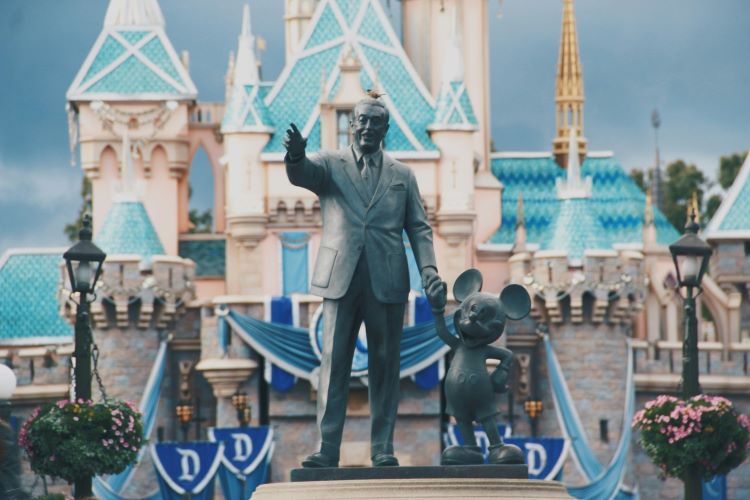 A decorative statue in front of the iconic Disneyland castle featuring Walt Disney and Mickey Mouse.