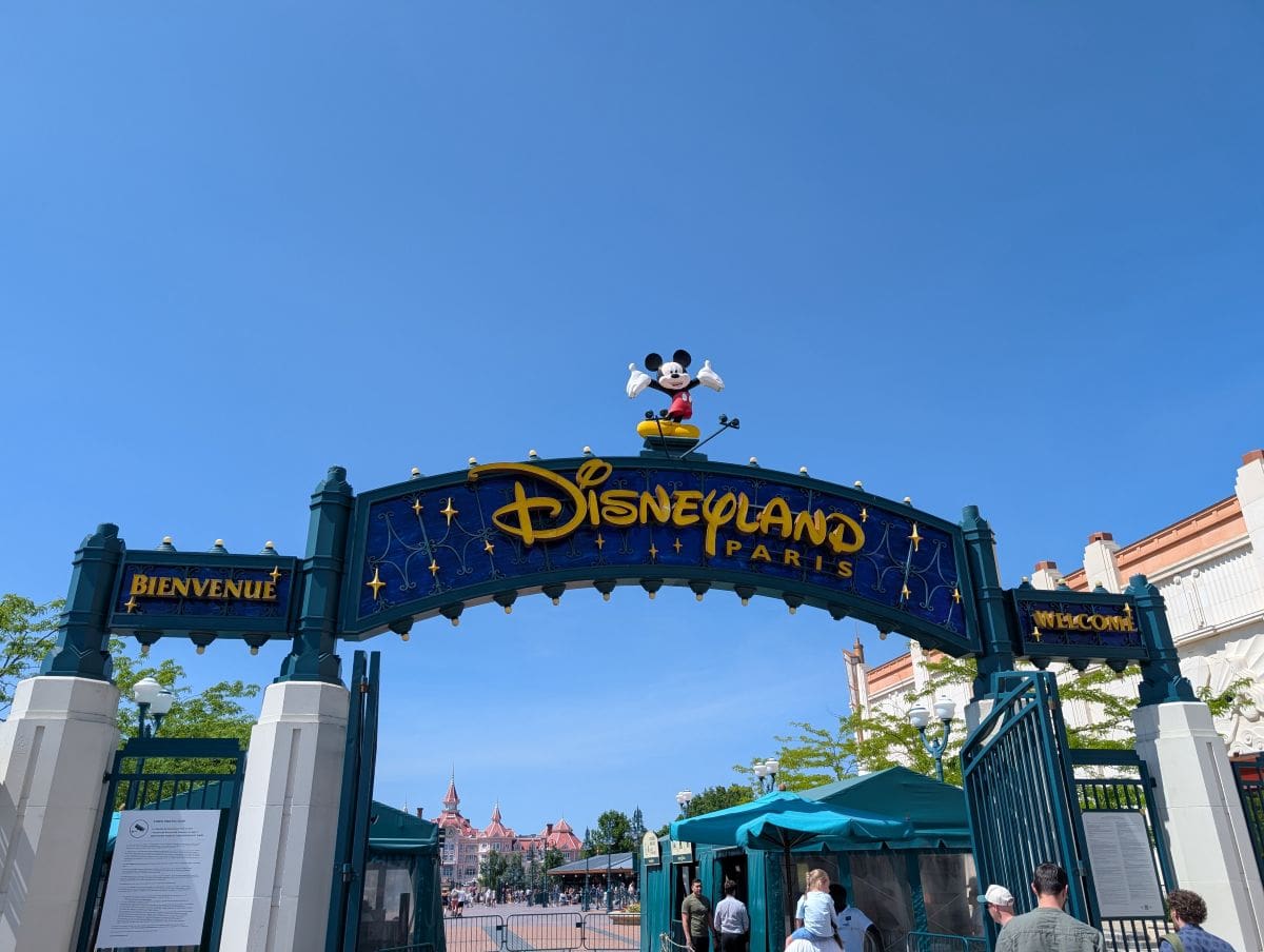 The large blue and gold archway entrance to Disneyland Paris's Disney Village, with a Mickey Mouse statue on top and a clear blue sky above.