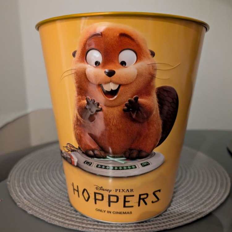A yellow tin popcorn bucket for the movie Hoppers, featuring a high-quality render of Mabel the beaver sitting on a digital mind-transfer pad. The Vue cinema exclusive bucket has the "Disney Pixar Hoppers" logo at the bottom.