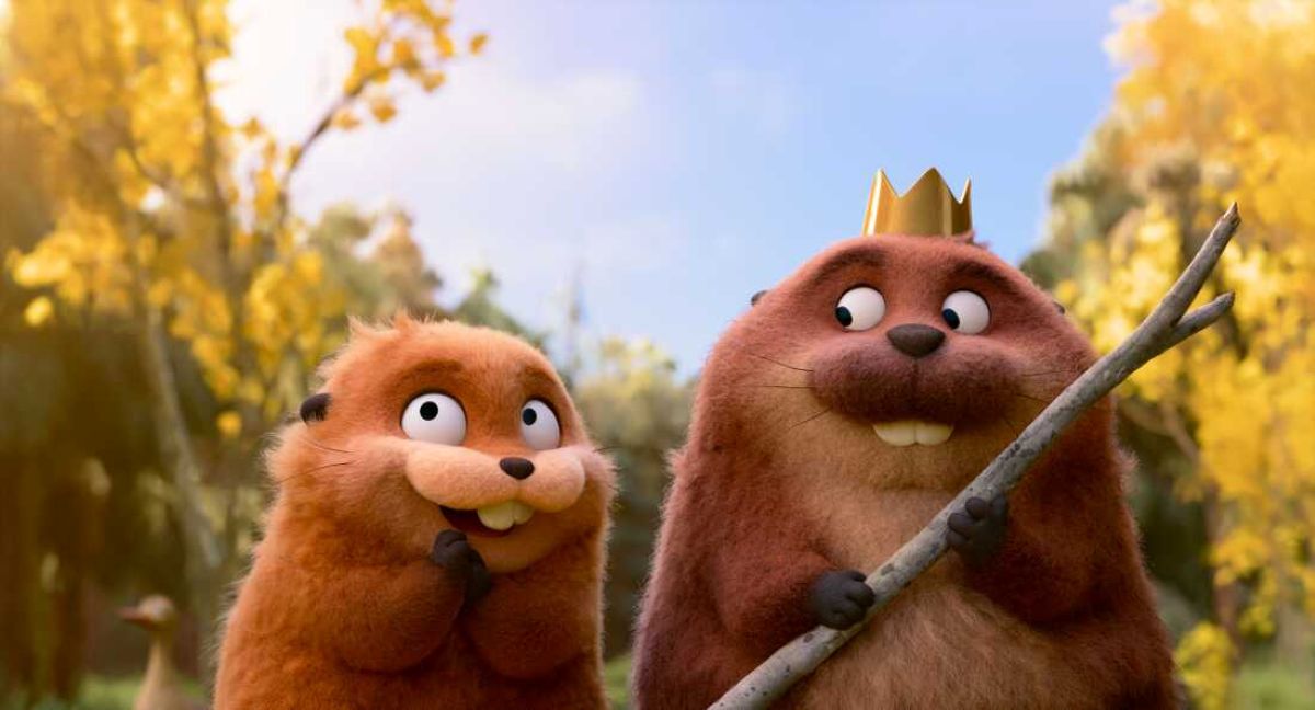 Two fluffy brown beavers from Pixar’s Hoppers stand in a vibrant forest setting; the larger beaver on the right wears a small gold crown and holds a wooden staff, while the smaller beaver on the left looks up with a wide, excited grin.