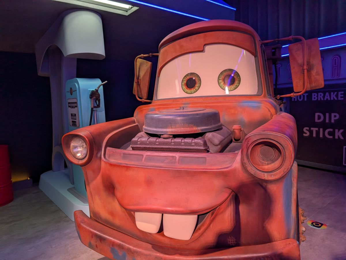 A full-scale, detailed model of Tow Mater from the movie Cars, parked in a neon-lit Flo's V8 Café setting with his hood open to reveal the engine.