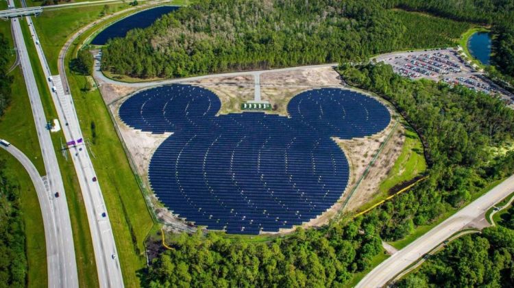 An aerial view of a massive solar panel farm arranged in the shape of a Mickey Mouse head surrounded by Florida trees and a highway.