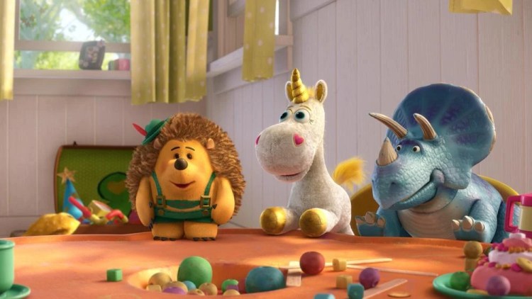Mr. Pricklepants the stuffed hedgehog wearing green lederhosen and a Tyrolean hat, standing on a table next to Buttercup the unicorn and Trixie the triceratops.